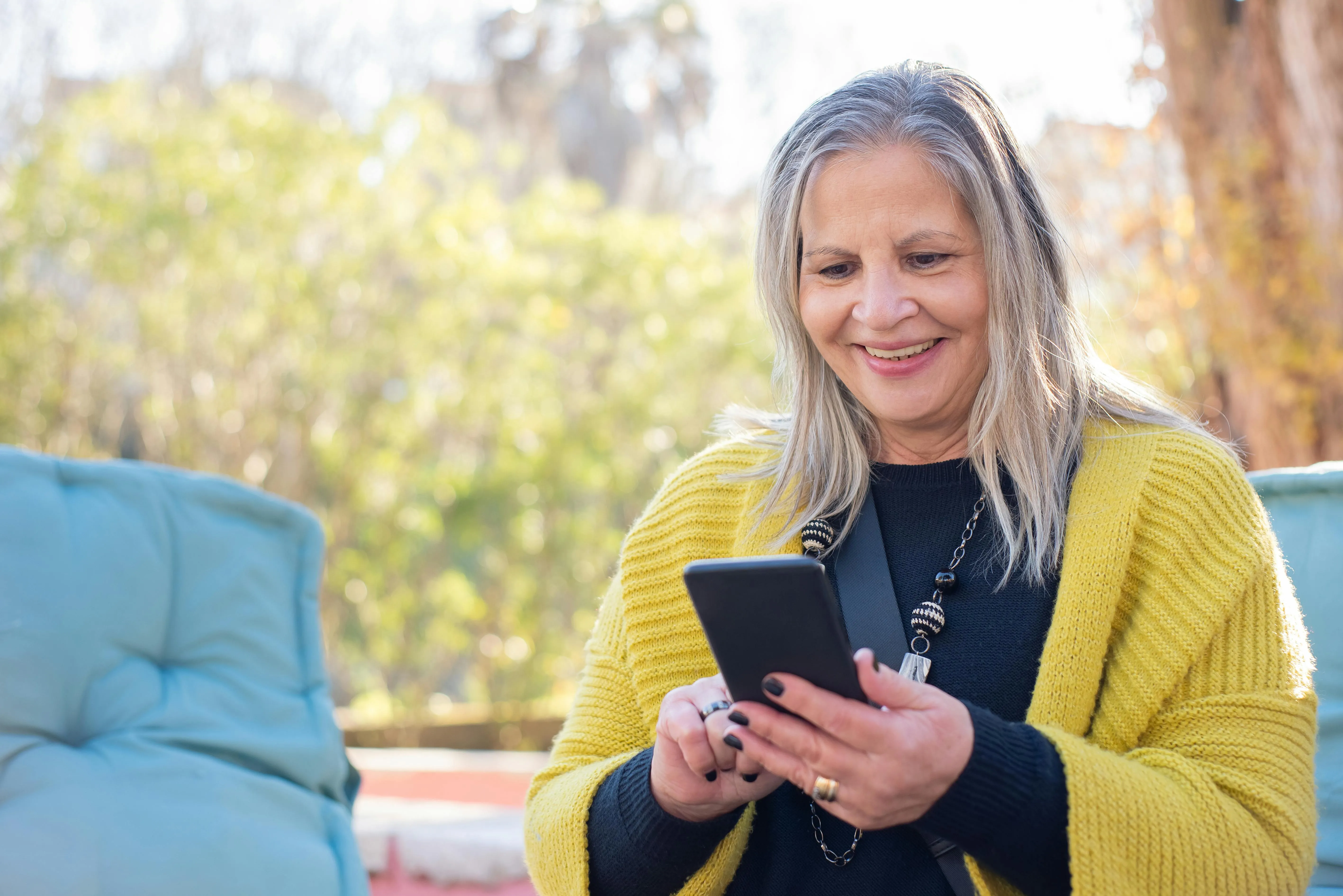 Mulher sorrindo usa celular ao ar livre em dia ensolarado