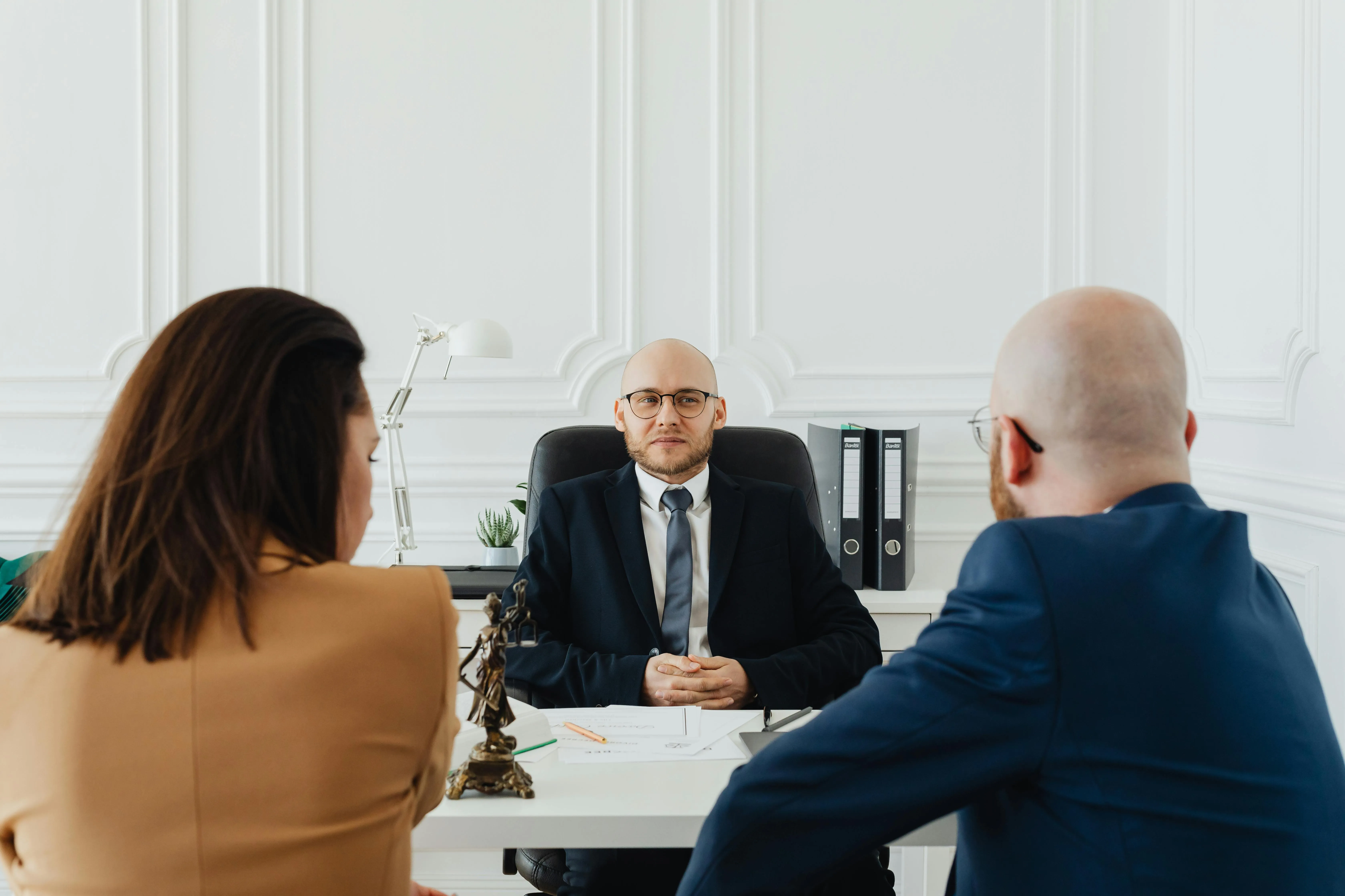 #FotoDescrição: Advogado sentado à mesa em reunião com clientes, representando atendimento profissional e estratégia de negócios.