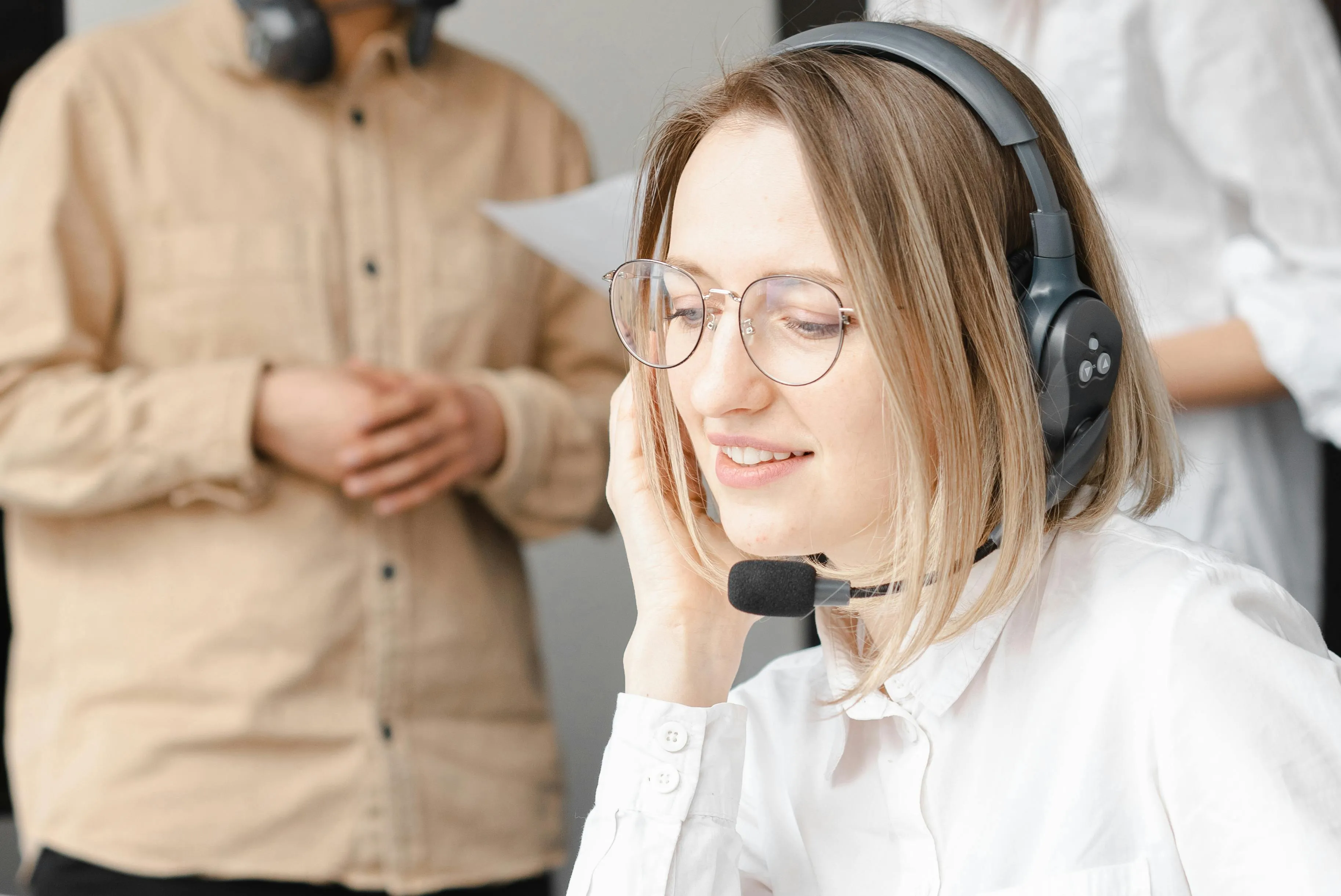 Mulher com headset atende chamada em ambiente de trabalho colaborativo.