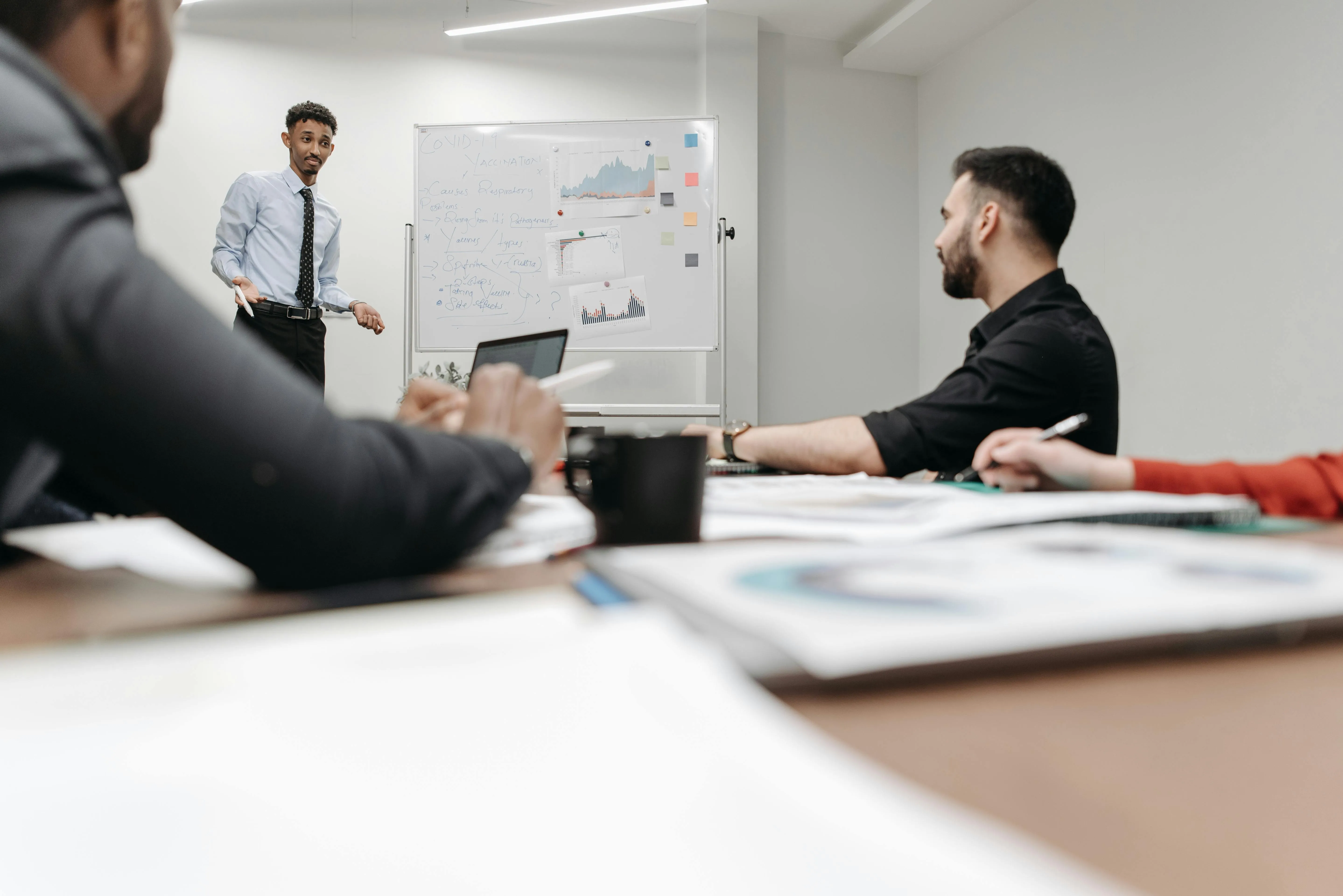 #FotoDescrição Profissional apresentando dados e gráficos em um quadro branco para uma equipe em reunião, com foco em análise de resultados, estratégias de vendas e geração de leads.