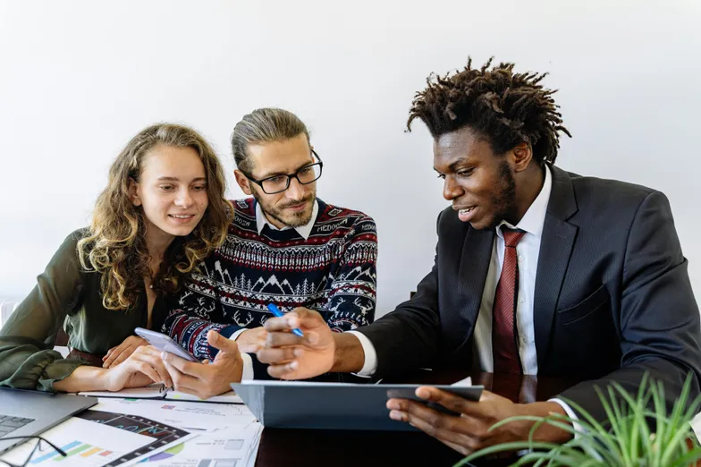#FotoDescrição: Três pessoas reunidas em uma mesa de escritório, analisando dados e gráficos enquanto discutem estratégias de fidelização no setor automotivo.