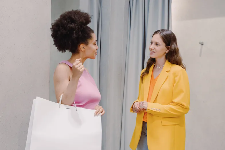Duas mulheres conversando, uma segurando uma sacola de compras.