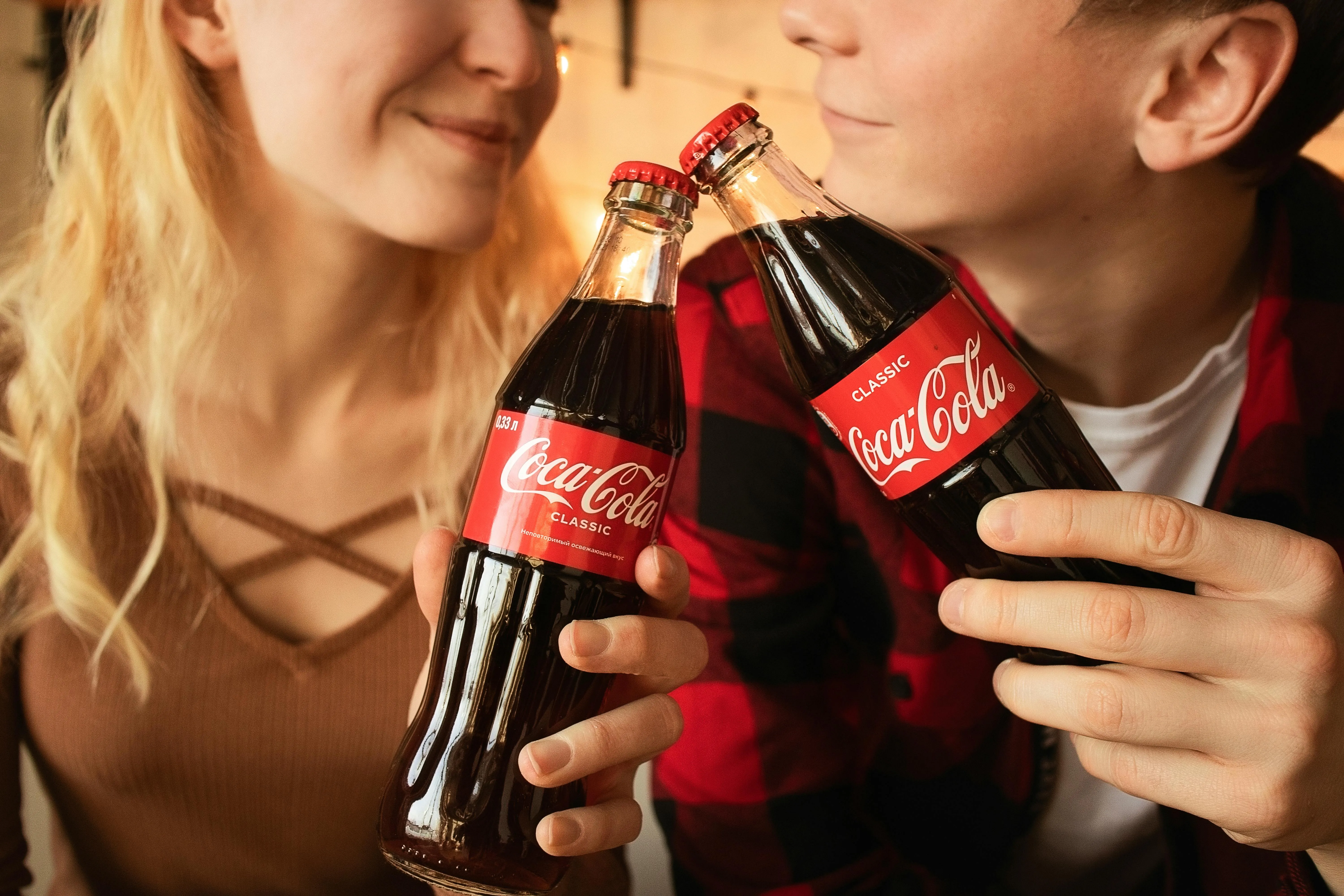 #FotoDescrição: Casal segurando garrafas de Coca-Cola, brindando e sorrindo, simbolizando conexão e momentos compartilhados.