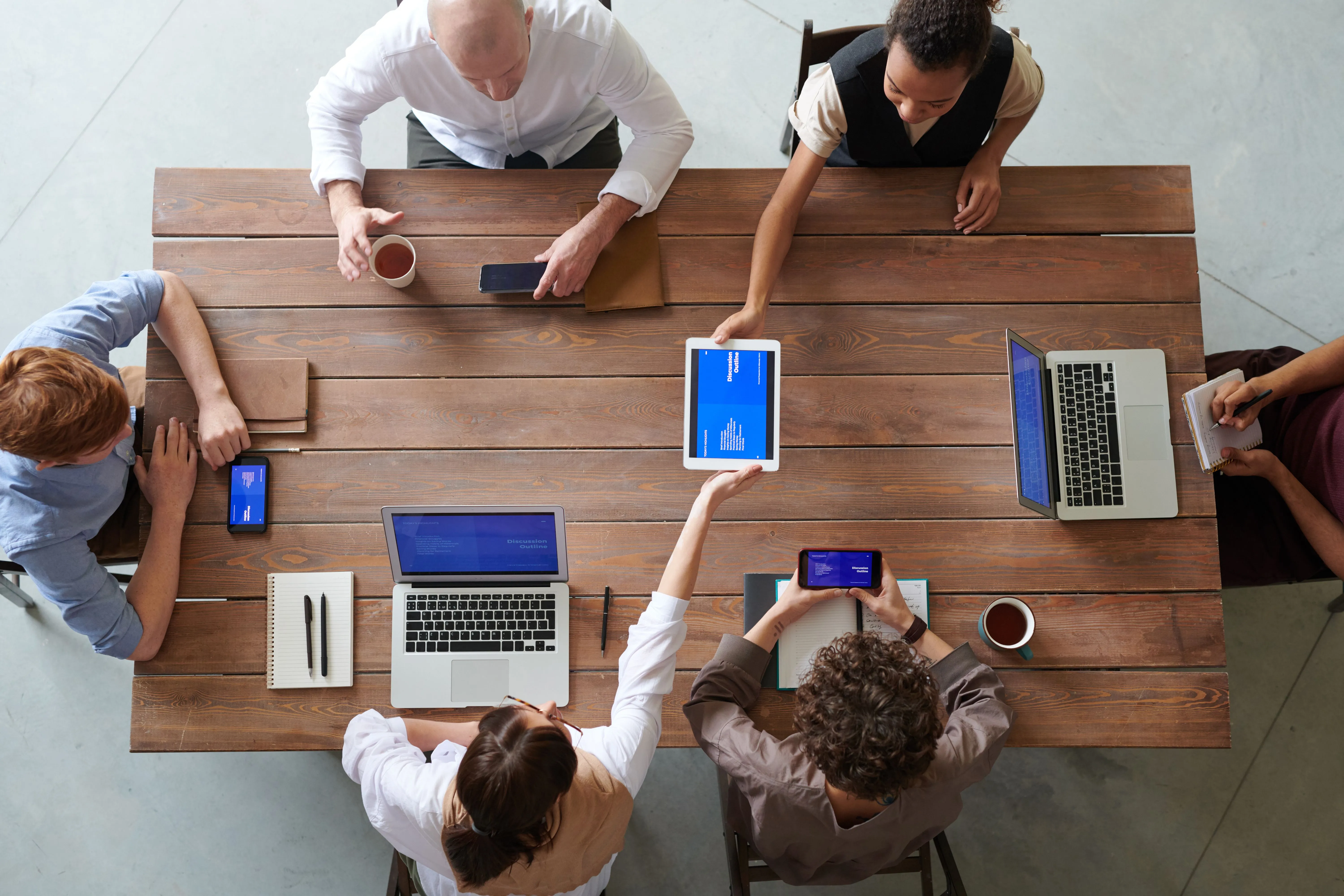 Equipe reunida em mesa com notebooks e tablet durante reunião de trabalho.