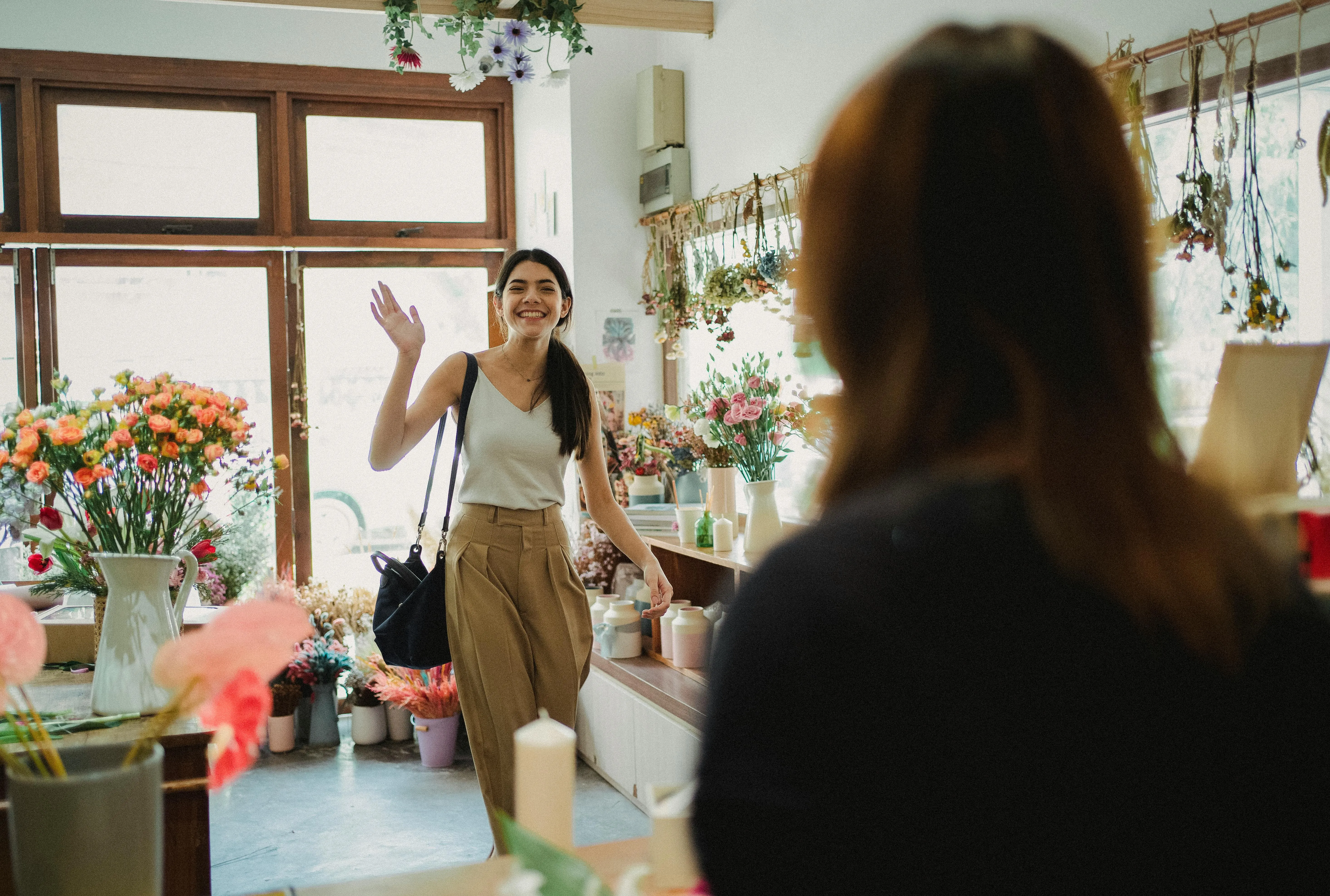 Mulher sorrindo acena ao entrar em loja de flores.