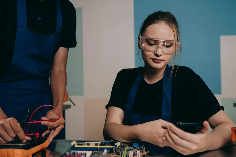 Técnicos trabalhando com eletrônica; mulher usa celular com óculos de proteção