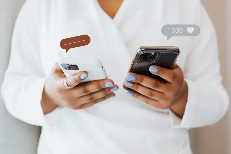 Pessoa segura dois celulares com ícones de interação em redes sociais.