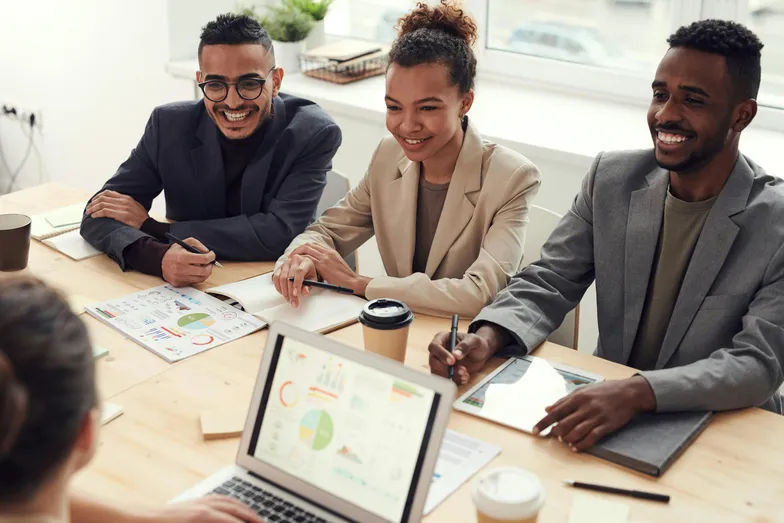 Pessoas sorrindo em reunião com gráficos e laptop sobre a mesa.