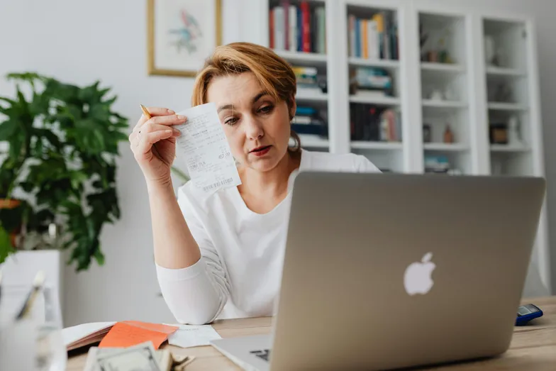 Mulher analisando recibo e finanças pessoais em frente ao notebook.