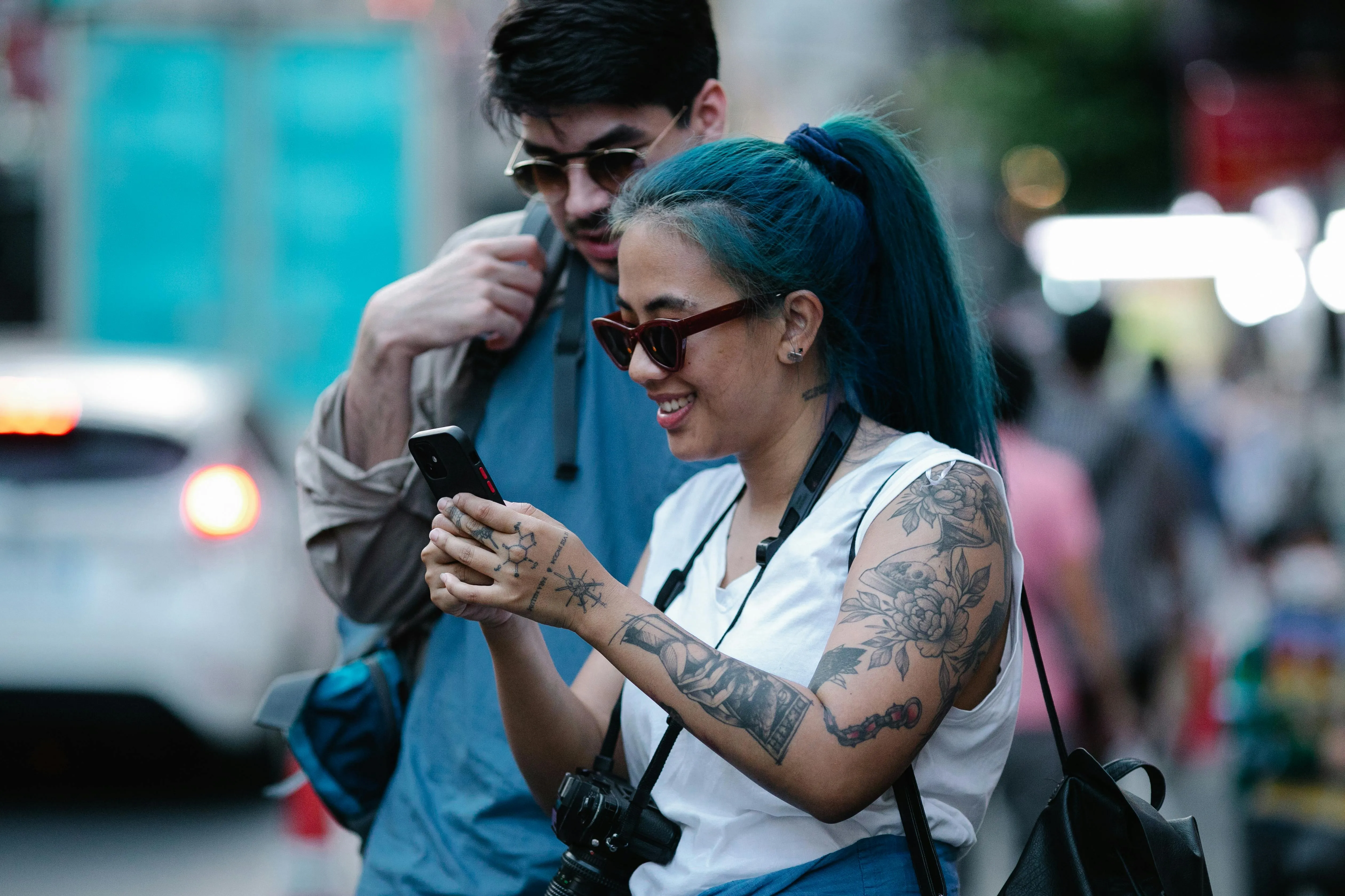 Mulher com tatuagens usando celular em rua com homem ao fundo