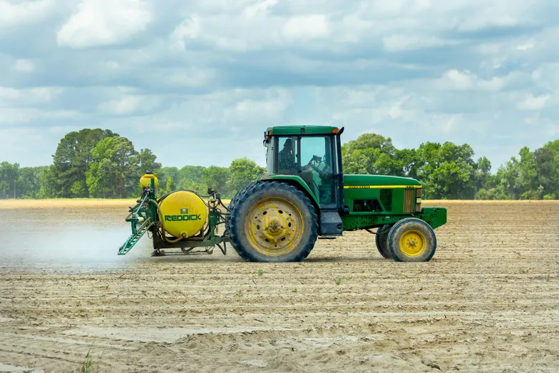 Trator pulverizando plantação em campo sob céu nublado