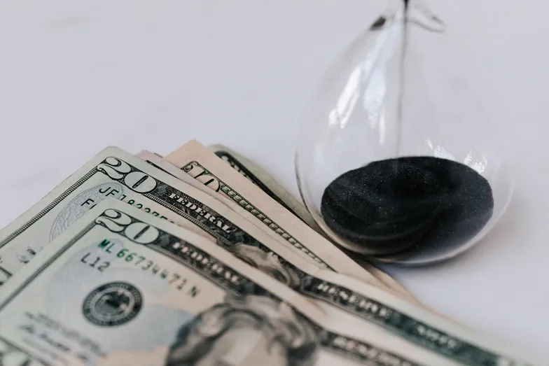 Notas de dólar ao lado de ampulheta simbolizando tempo e dinheiro