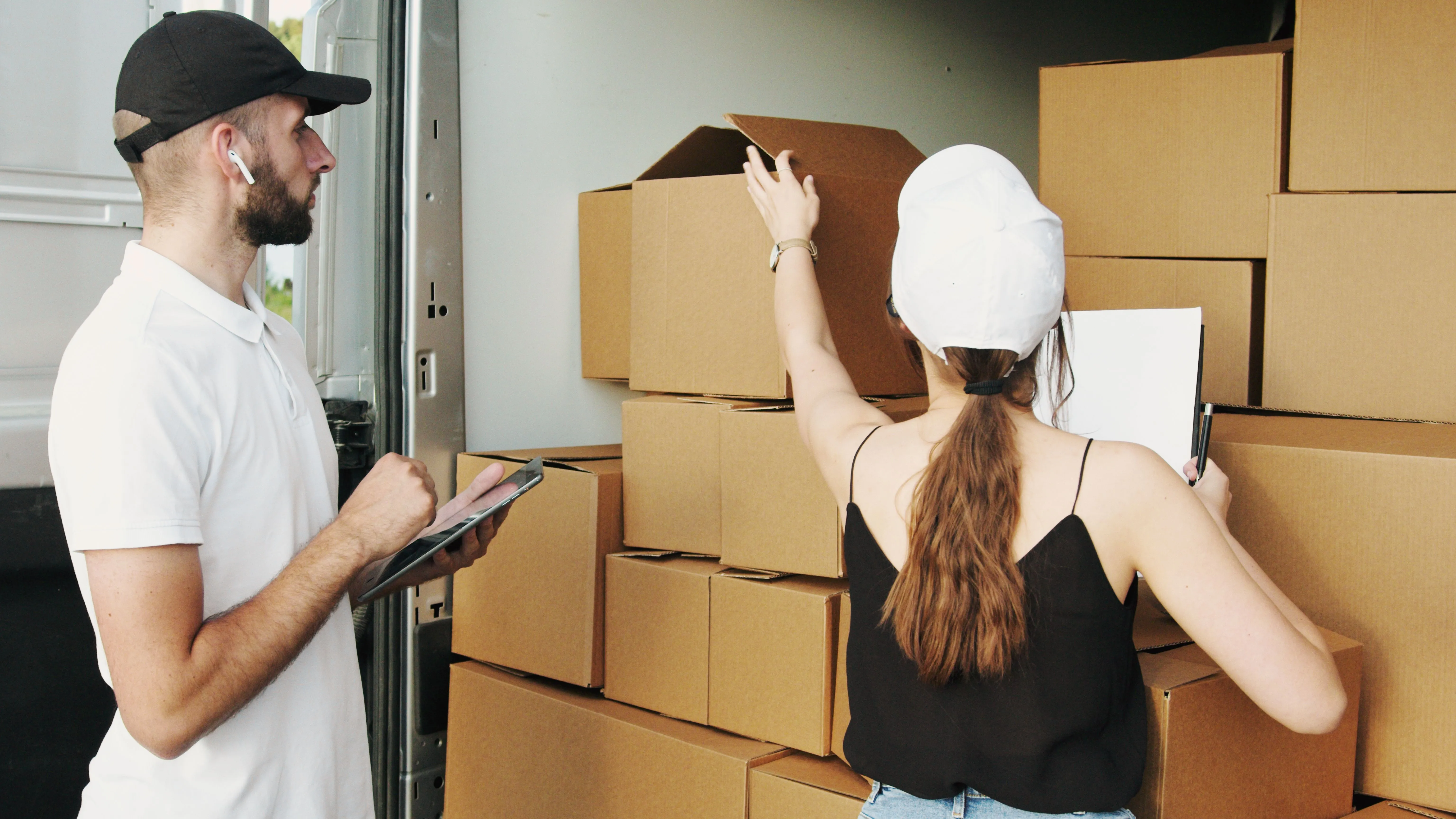 Dois trabalhadores organizam caixas dentro de um veículo de carga.