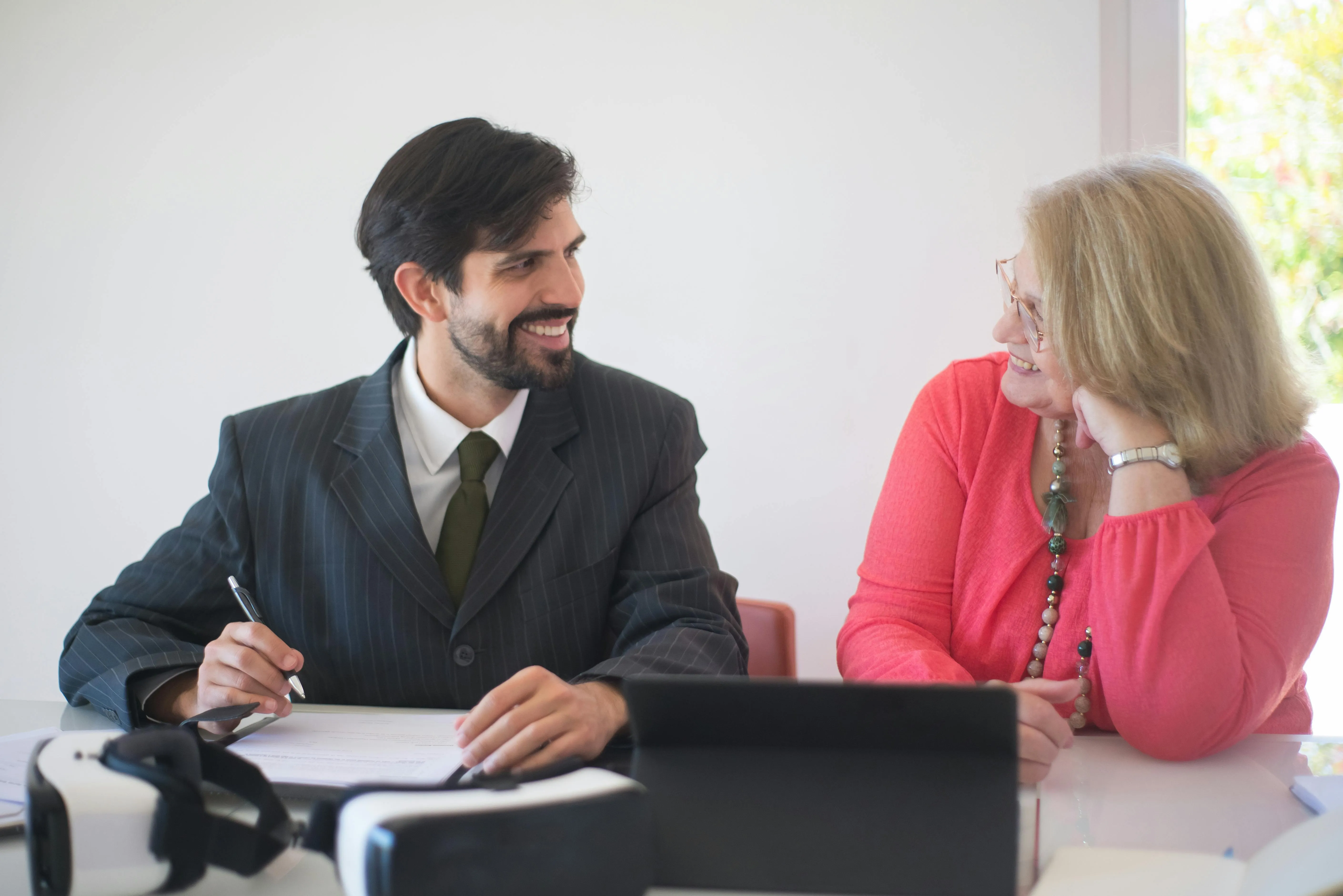 Homem de terno conversa sorrindo com mulher durante reunião à mesa